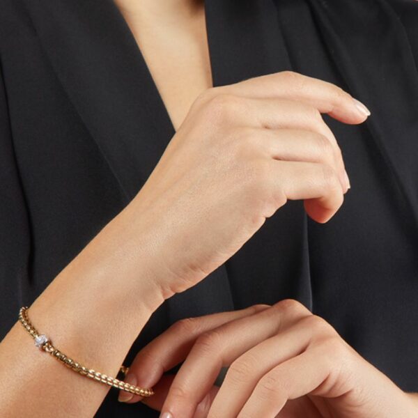 bracelet fope eka en or jaune et diamants porté par une femme habillée en noir qui tire légèrement dessus pour montrer qu'il est flexible