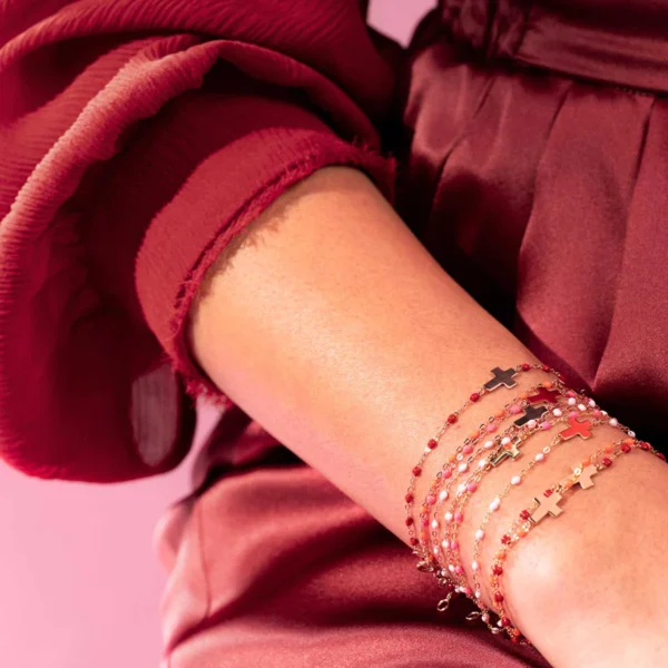 bracelets gigi clozeau motif croix en or rose et résine rose, rouge, blanc, portés en accumlation par une femme vêtue de rouge