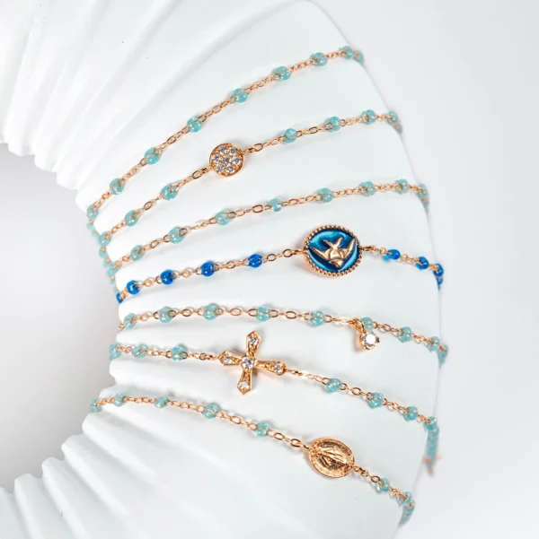 présentoir gigi clozeau blanc avec plusieurs bracelet en or rose et résine aqua avec motif diamants, poisson, madone, croix vintage