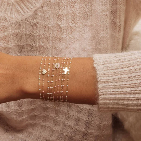 poignet de femme portant un pull en maille clair orné de plusieurs bracelets gigi clozeau dans les tons de blanc beige et rose avec et sans motifs et diamants