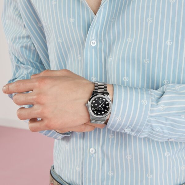 montre gucci timless fond onyx abeilles portée par un homme habillée d'une chemise gucci bleu rayée blanche