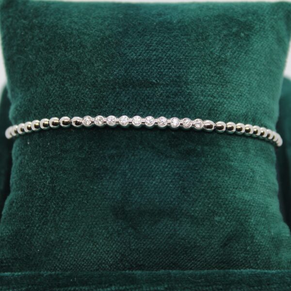 Bracelet création Valer en or blanc, composé de petites boules dont certaines serties de diamants. Présenté sur un coussin vert.