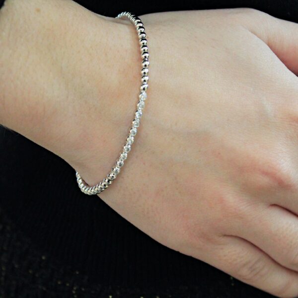 Bracelet création Valer en or blanc, composé de petites boules dont certaines serties de diamants, porté par une femme habillée en noir, zoom sur sa main.