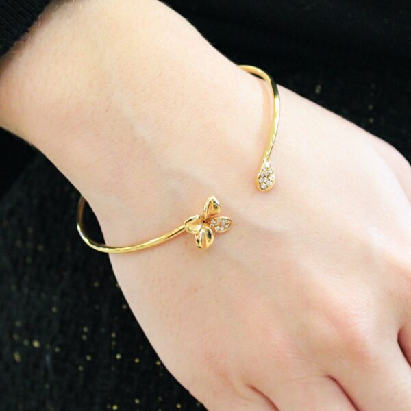 Bracelet jonc, création Valer en or rose 18 carats et diamants, motif fleur d'un côté et pétale de l'autre. Porté sur une main de femme habillée en noir