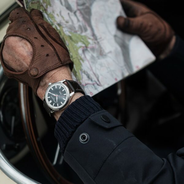 Montre Frédérique Constant Classics Vintage Rally Healey portée au poignet d'un homme portant des gants en cuir et tenant une carte